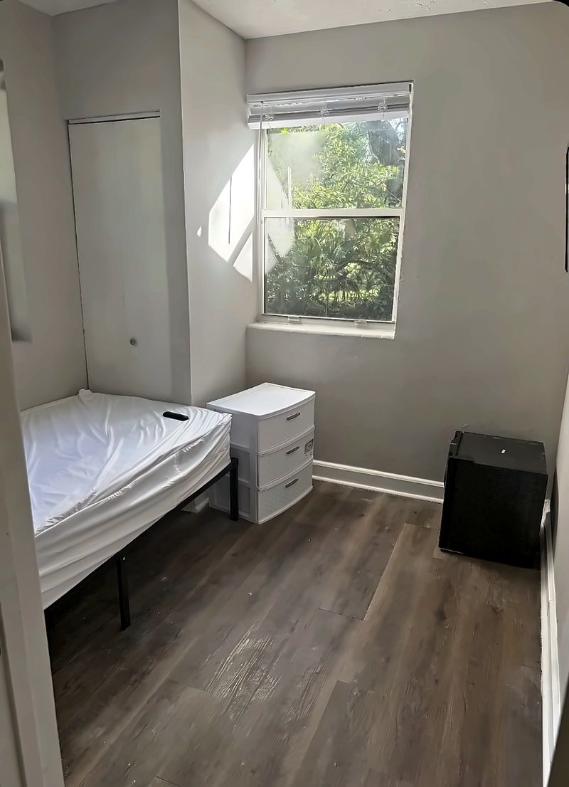 Sunny bedroom with a bed, a drawer unit, and a mini fridge