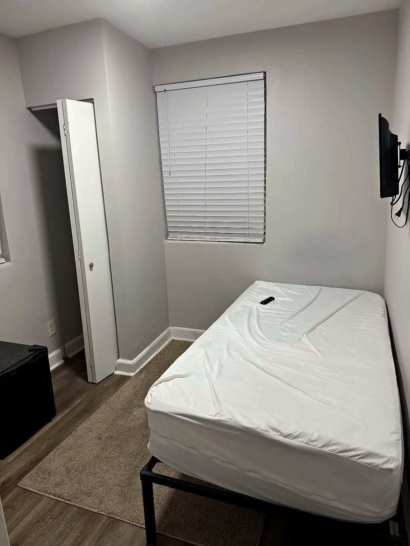 Bedroom with a bed, a wall-mounted TV, a mini fridge, and a rug