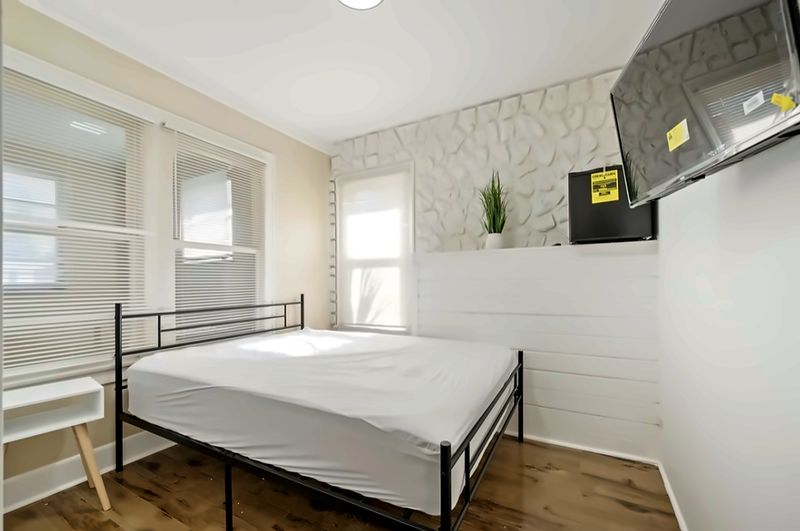 Smaller bedroom with a textured stone accent wall, mini fridge, and wall-mounted TV